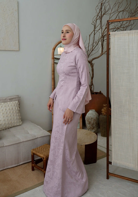 Woman in a light pink traditional outfit standing in a room with a couch and decorative items.