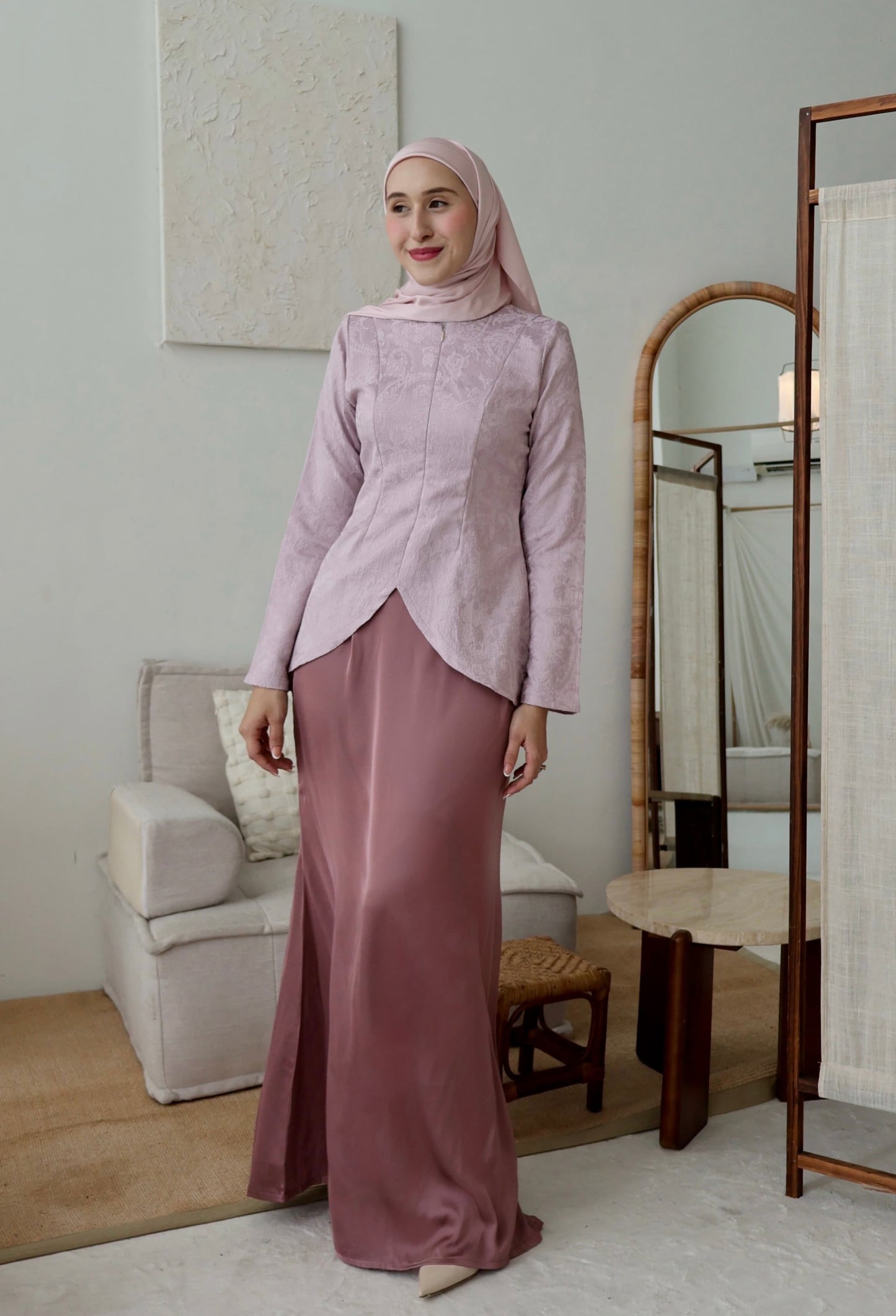 Woman in a pink traditional outfit standing in a room with a mirror and furniture.