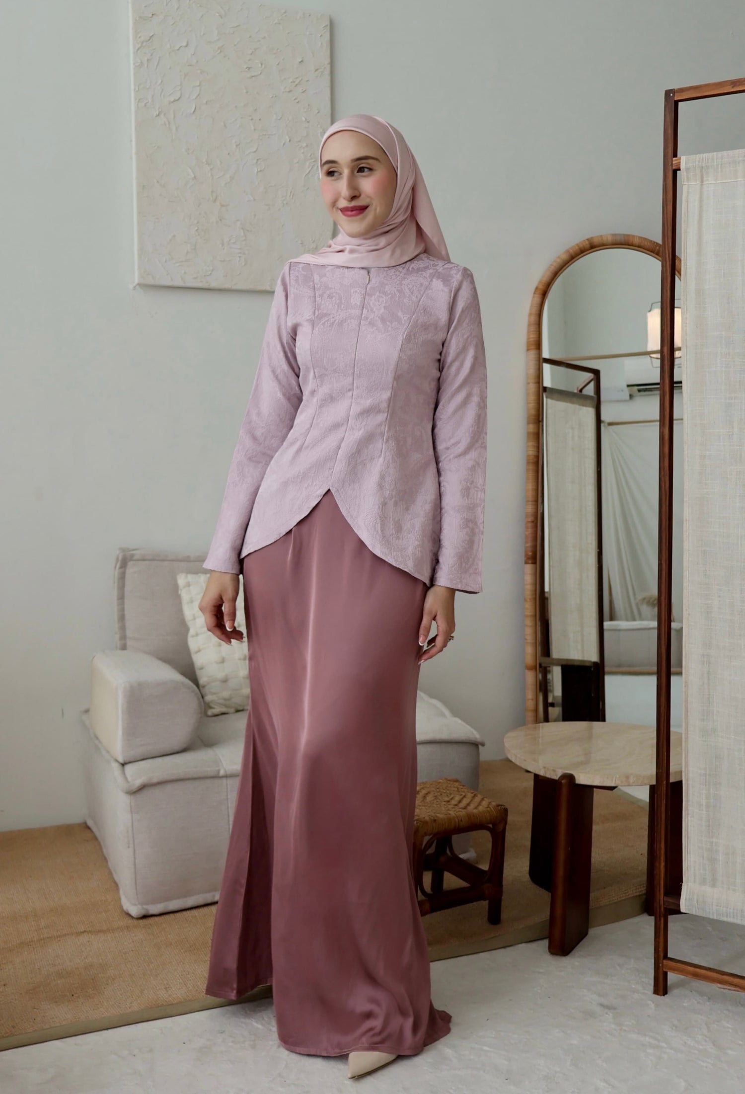 Woman in a pink traditional outfit standing in a room with a mirror and furniture.