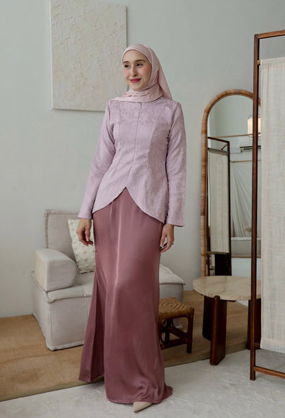 Woman in a pink traditional outfit standing in a room with a mirror and furniture.